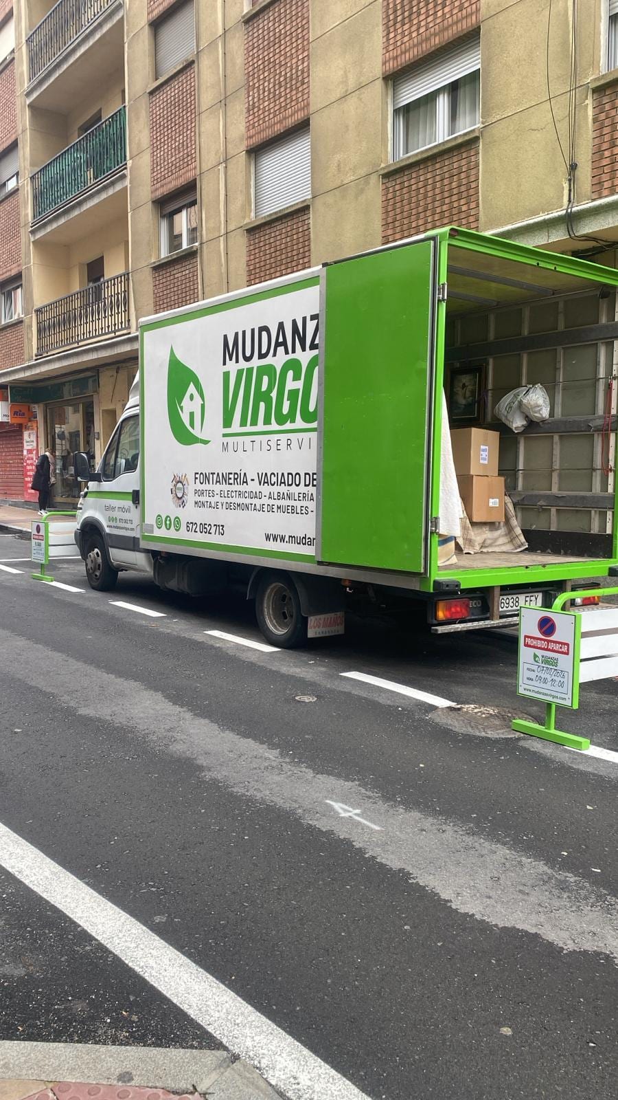 Camión verde rotulado de Mudanzas Virgos aparcado en una zona reservada para carga, con la caja abierta y cajas de cartón dentro