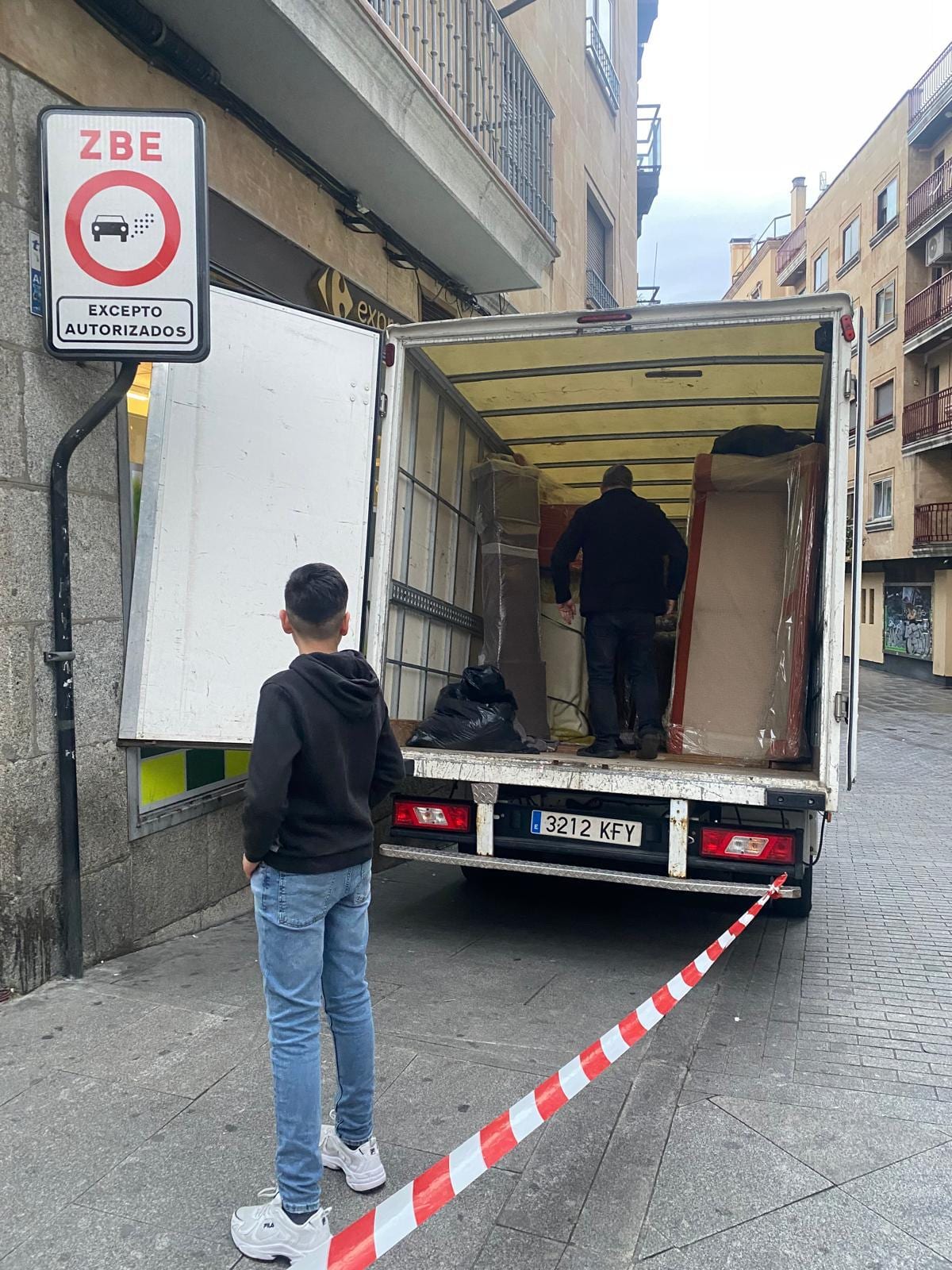 Carga de un camión de mudanza en una calle peatonal balizada con cinta, junto a una señal de zona de bajas emisiones