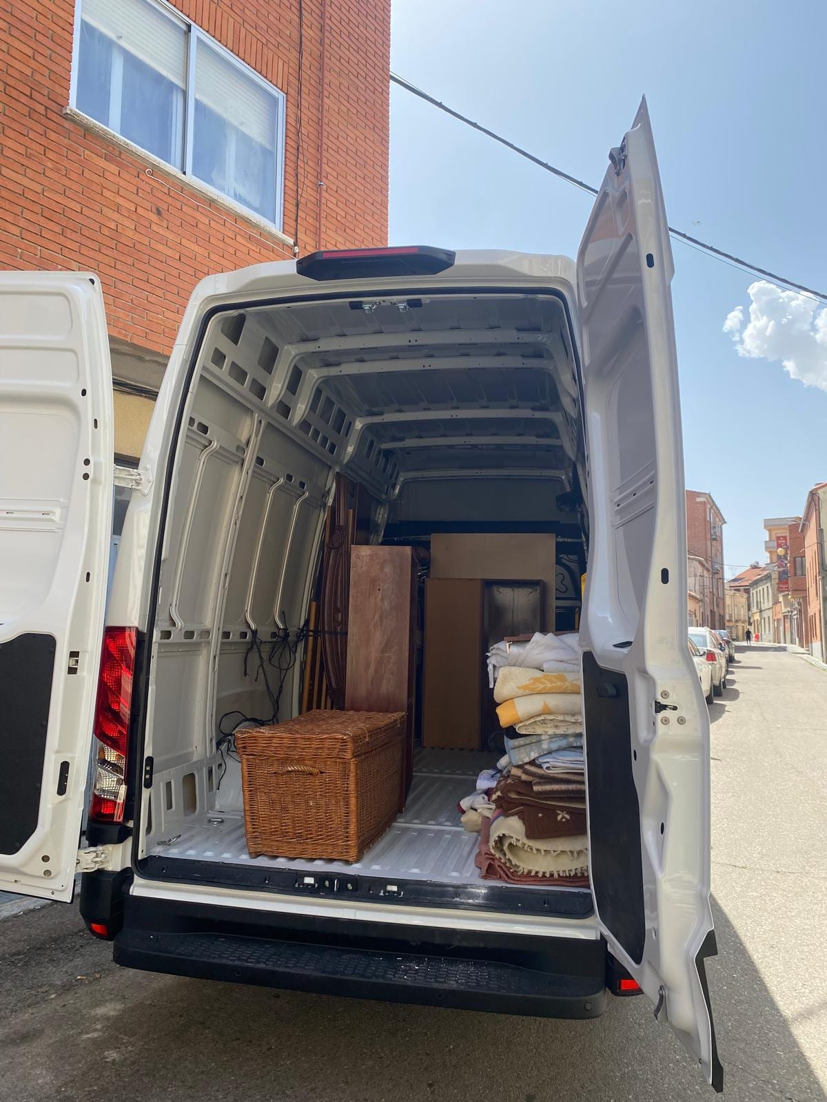 Furgoneta con las puertas traseras abiertas, cargada con un arcón de madera, muebles y bultos protegidos con mantas
