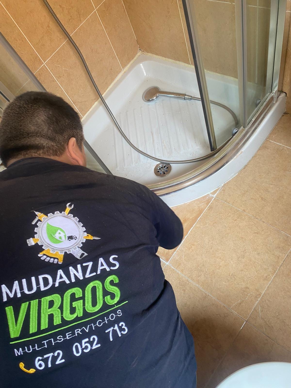 Fontanero sellando el perímetro de un plato de ducha blanco con mampara curva